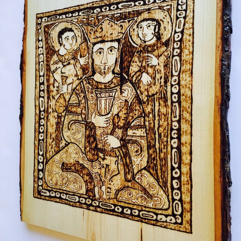 May include: A woodburned image of a king with a crown, holding a scepter, and two figures standing behind him. The image is framed with a decorative border.