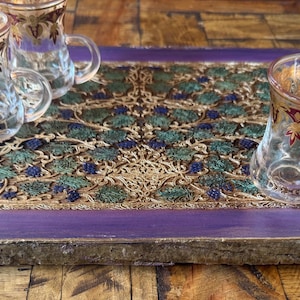 May include: A purple wooden tray with a gold and green patterned inlay. Three clear glass cups with gold and red accents are on the tray.