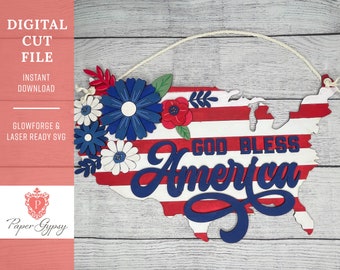 May include: A wooden cutout of the United States of America with red and white stripes and the words "God Bless America" in blue. The cutout is decorated with blue and white flowers.