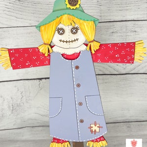 May include: A wooden scarecrow with a green hat, yellow hair, red and white polka dot sleeves, and a blue dress with buttons and pockets. The scarecrow has a stitched smile and X-shaped eyes.
