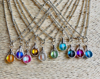 May include: A set of 12 silver necklaces with iridescent glass teardrop pendants. Each pendant is wrapped in silver wire and hangs from a delicate silver chain.