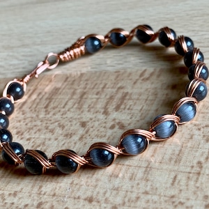 May include: A copper wire wrapped bracelet with gray and black gemstone beads.