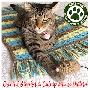 May include: A brown tabby cat with green eyes lies on a crocheted blanket with blue, brown, and yellow stripes. The blanket has fringe on the edges. The cat is playing with a crocheted brown catnip mouse. The image has a green circle with a paw print and the text "Kitty Cat Tested Loved Approved".