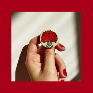 May include: A white ceramic pin with a red carnation flower design.