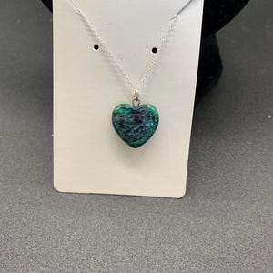 May include: A silver chain necklace with a green and black heart-shaped pendant.