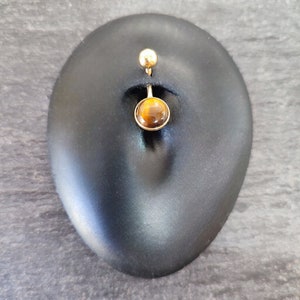 May include: Gold belly button ring with a round tiger's eye gemstone.