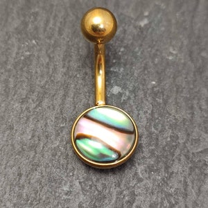 Peut inclure: Anneau de nombril en or avec une incrustation ronde en nacre d'ormeau. La nacre présente un motif iridescent vert, bleu et rose.