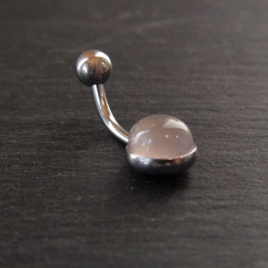 Puede incluir: Un piercing de ombligo plateado con una piedra preciosa rosa clara.