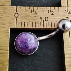 Peut inclure: Un anneau de nombril violet et blanc avec une pierre ronde, plate et semblable &agrave; un bijou. L'anneau est mesur&eacute; &agrave; l'aide d'une r&egrave;gle.