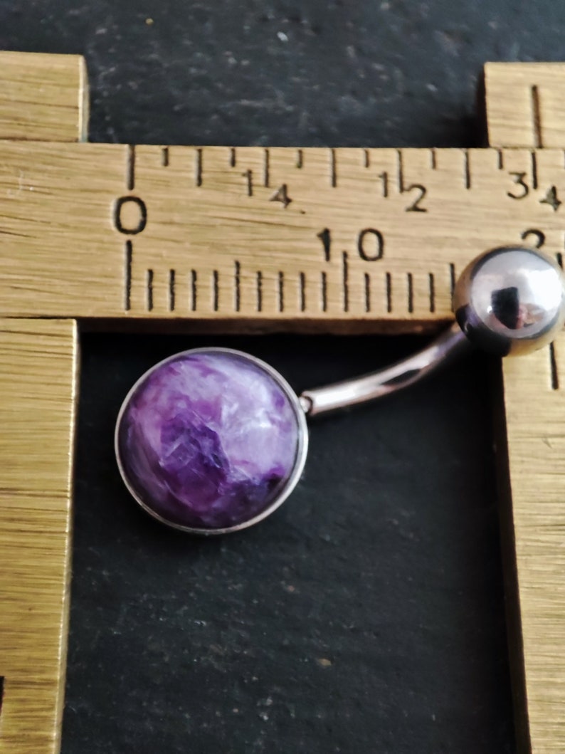 Peut inclure: Un anneau de nombril violet et blanc avec une pierre ronde, plate et semblable &agrave; un bijou. L'anneau est mesur&eacute; &agrave; l'aide d'une r&egrave;gle.