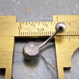 May include: A silver belly button ring with a clear, round gemstone. The ring is measured with a caliper, showing a length of 10 millimeters.