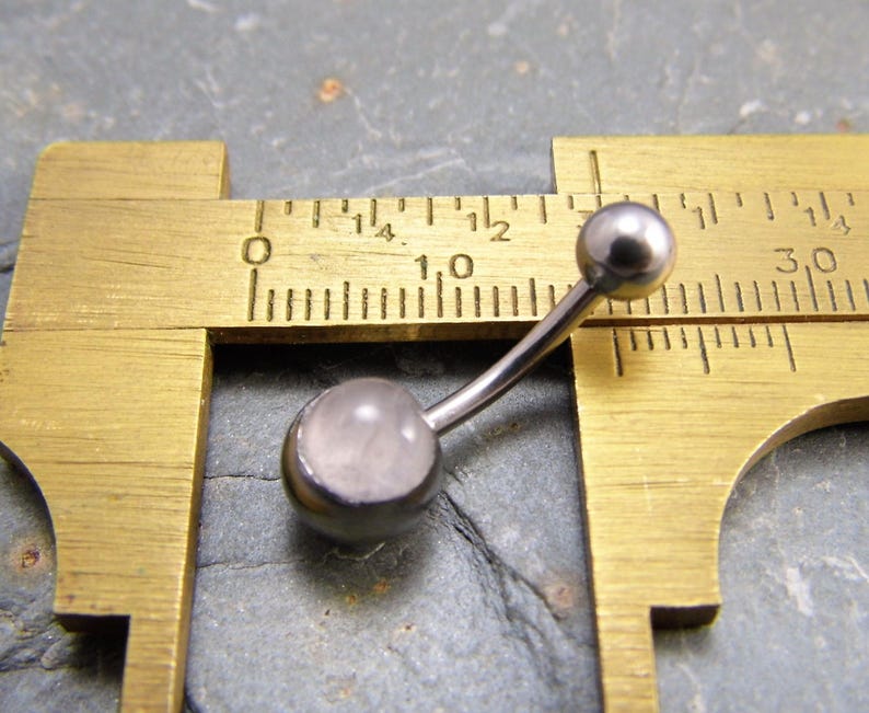 May include: A silver belly button ring with a clear, round gemstone. The ring is measured with a caliper, showing a length of 10 millimeters.