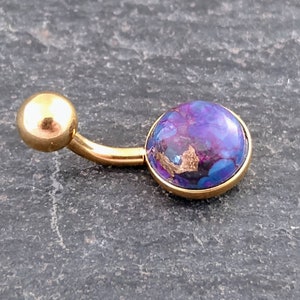 Puede incluir: Anillo de ombligo dorado con una piedra morada y azul.