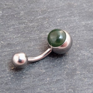 Puede incluir: Un piercing de ombligo de plata con una piedra preciosa verde en el centro.