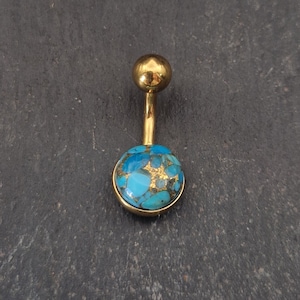 Könnte beinhalten: Ein goldfarbener Bauchnabelpiercing mit einem türkis- und goldfarbenen Stein. Die oberen und unteren Kugeln sind rund. Der Stein ist ein leuchtendes Blau mit Goldflecken.