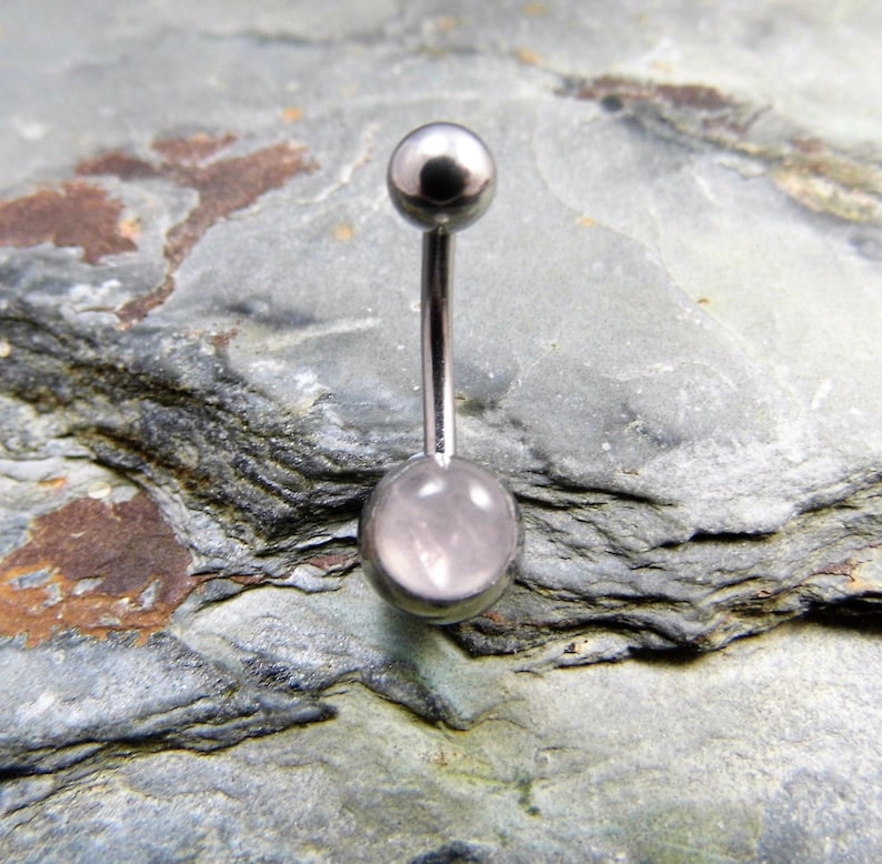 May include: A silver belly button ring with a clear pink stone in the center.