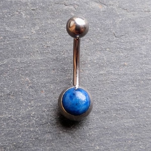 Peut inclure: Un piercing de nombril en argent avec une pierre précieuse bleue. Le piercing est en acier chirurgical et est un choix populaire pour les piercings corporels.