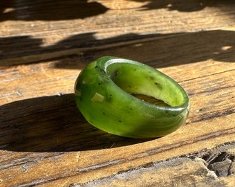 May include: A green jade ring with a smooth, polished finish. The ring has a wide band and a slightly oval shape.