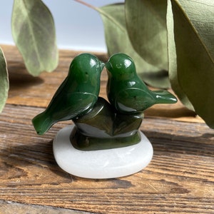 May include: A green jade sculpture of two birds kissing, perched on a white jade base.