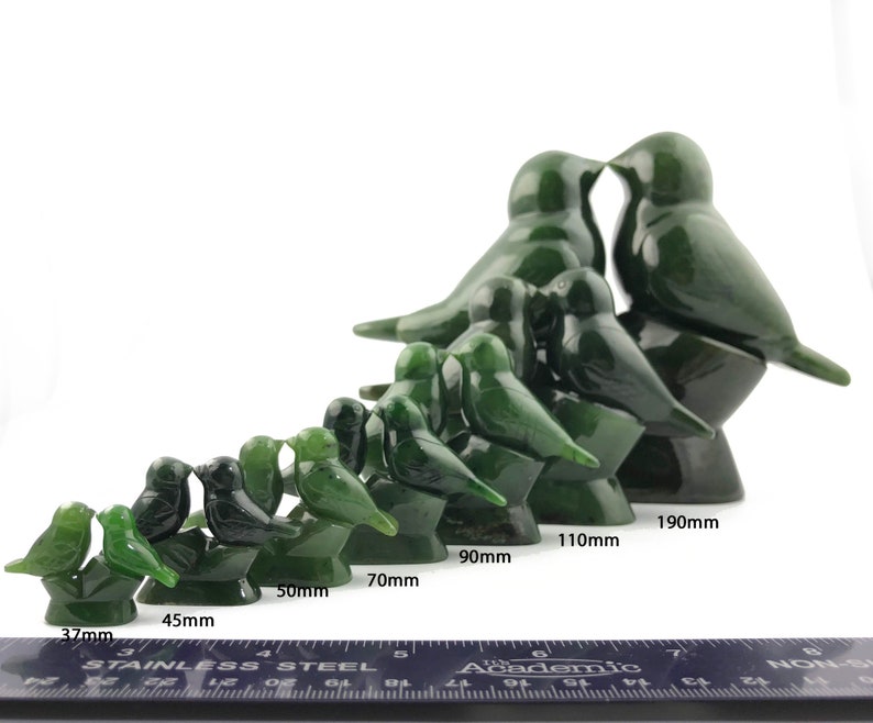 Puede incluir: Un conjunto de 10 esculturas de p&aacute;jaros de jade verde en varios tama&ntilde;os, que van desde 37 mm hasta 190 mm. Los p&aacute;jaros est&aacute;n tallados en una pose de beso, con los p&aacute;jaros m&aacute;s grandes de pie sobre una base y los p&aacute;jaros m&aacute;s peque&ntilde;os posados ​​en sus espaldas. Las esculturas est&aacute;n dispuestas en una l&iacute;nea desde la m&aacute;s peque&ntilde;a hasta la m&aacute;s grande, con una regla debajo para referencia de tama&ntilde;o.