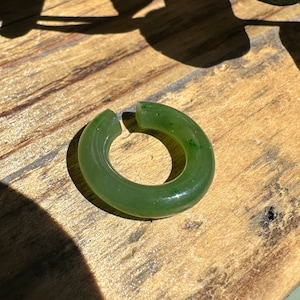 Può includere: Un anello di giada verde con una finitura liscia e lucida. L'anello è spesso e ha una forma arrotondata.