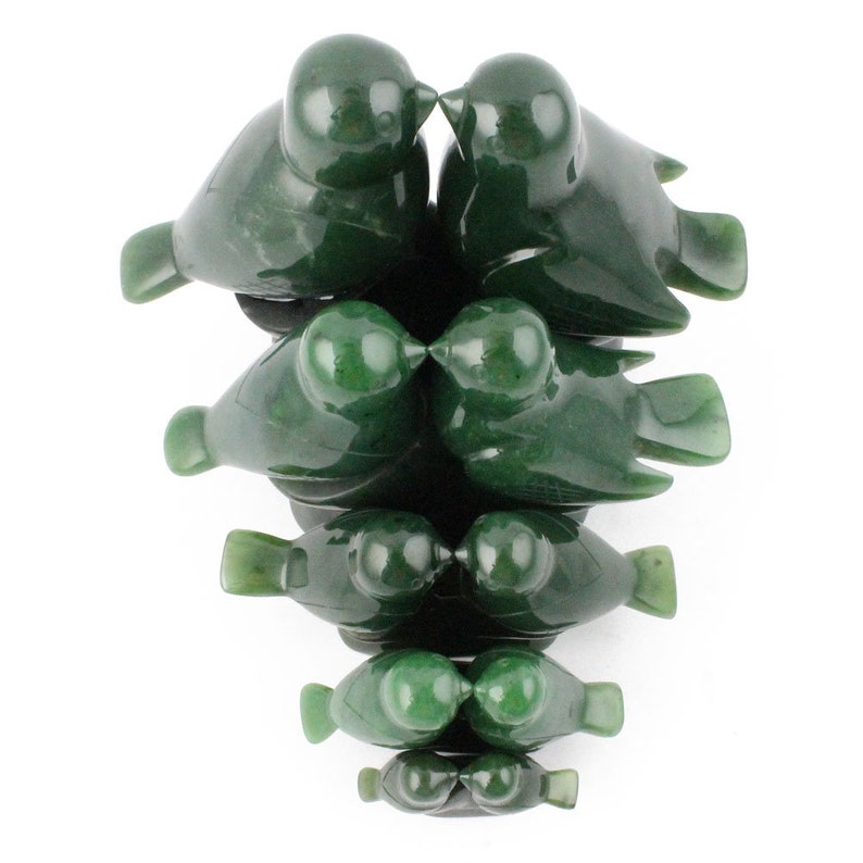 Puede incluir: Un conjunto de siete esculturas de p&aacute;jaros de jade verde, cada una de un tama&ntilde;o diferente, dispuestas en una pila con los p&aacute;jaros m&aacute;s grandes en la parte superior y los m&aacute;s peque&ntilde;os en la parte inferior. Los p&aacute;jaros est&aacute;n tallados en un estilo realista y tienen sus picos toc&aacute;ndose, como si se estuvieran besando.