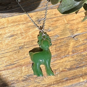 May include: A jade green deer pendant necklace on a silver chain. The deer is carved in a standing position with its head tilted up.