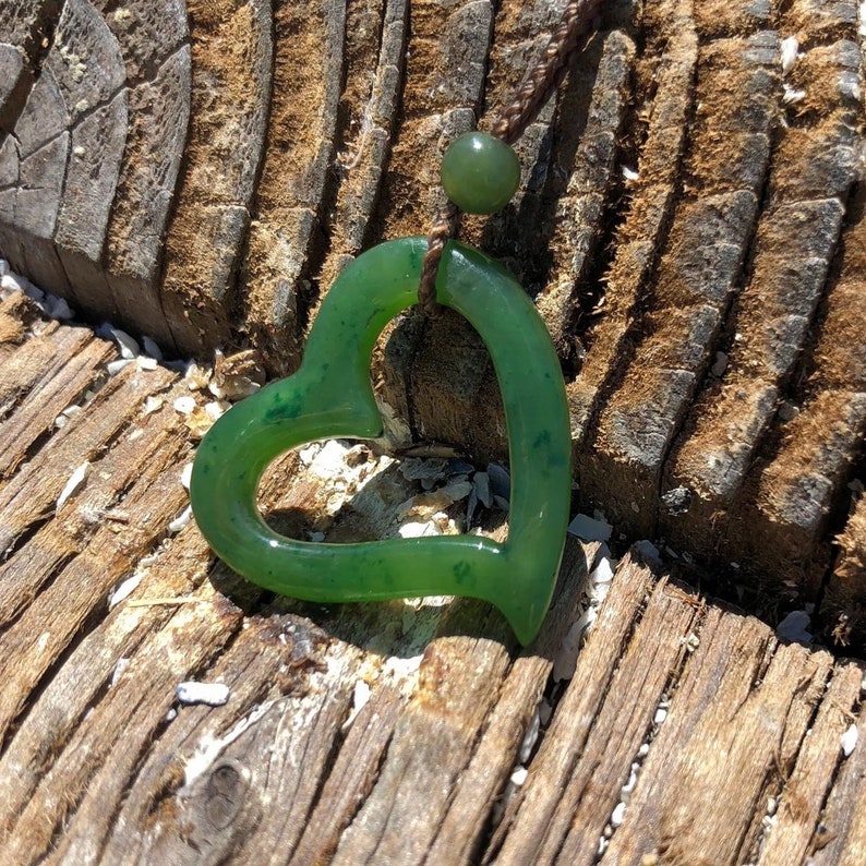 May include: A green jade heart pendant necklace. The heart is carved from jade and has a smooth, polished finish. The necklace is made of brown cord.