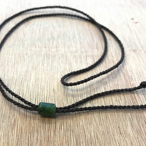 May include: A dark brown cord necklace with a single green jade bead.