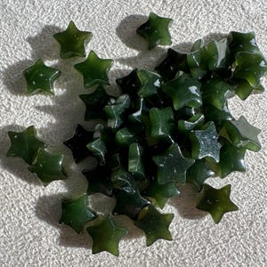 May include: A pile of dark green star-shaped beads. The beads are made of a smooth, polished stone.