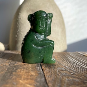 May include: A small, green jade sculpture of a seated monkey. The monkey is carved in a stylized, abstract style with simple features. The sculpture is smooth and polished.