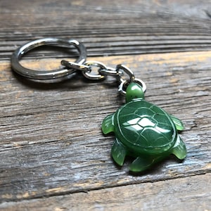 Puede incluir: Un llavero de tortuga de jade verde con un anillo y una cadena plateados.