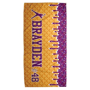 Peut inclure: Serviette de plage rectangulaire avec un motif de gaufre en arri&egrave;re-plan. Le nom "BRAYDEN" en violet, une silhouette de joueur de baseball et le num&eacute;ro "48" sont pr&eacute;sents. Un motif d&eacute;goulinant violet et blanc avec des vermicelles color&eacute;s est sur le c&ocirc;t&eacute; droit.