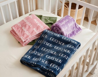 Könnte beinhalten: Eine Auswahl von vier weichen Decken in Marineblau, Rosa, Lila und Olivgrün. Jede Decke zeigt ein sich wiederholendes weißes Schriftmuster eines bestimmten Namens: Grayson, Harper, Sophia oder Cooper, das auf den Stoff gedruckt ist.