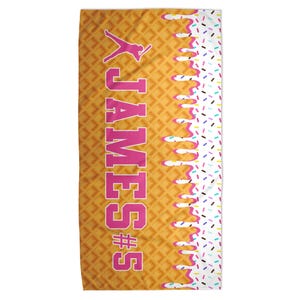 Peut inclure: Serviette rectangulaire &agrave; motif gaufr&eacute; avec le nom "JAMES" en rose et un num&eacute;ro. Le c&ocirc;t&eacute; droit pr&eacute;sente un motif d&eacute;goulinant blanc avec des vermicelles color&eacute;s. Le fond est de couleur marron clair.