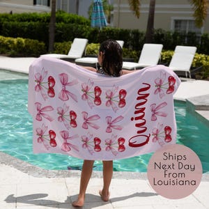 May include: Pink beach towel with a cherry and bow pattern. The towel has the name "Quinn" written in red on it.