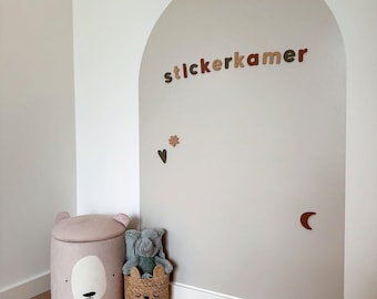 May include: A beige wall decal in the shape of an arch featuring the text "stickerkamer" in brown letters, accompanied by small brown star, heart, and moon stickers. Beside it sits a light pink bear-shaped storage bin and a woven basket.
