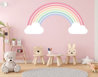 May include: A child's playroom with a pink wall featuring a large rainbow wall decal. The room includes a teddy bear, a small table, two animal-shaped chairs, and a gray rug. A wooden shelf and a toy airplane are also visible.