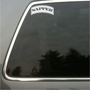 May include: A white rectangular sticker with the word "SAPPER" in a curved banner shape. The sticker is affixed to a car window, reflecting a blurred outdoor scene.