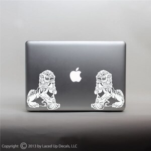 May include: A gray laptop with two white lion stickers on the back. The stickers are detailed with intricate designs. The Apple logo is visible. Copyright 2013 by Laced Up Decals, LLC.