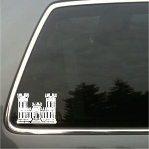 May include: White vinyl decal of a castle-like structure, possibly a military emblem, on a car window. The design shows two tall towers and a central building with detailed features. The decal is on the rear window of a vehicle.