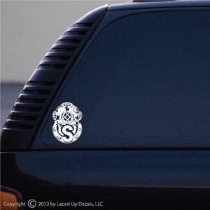 May include: White decal of a vintage diving helmet with the letter "S" in the center. The decal is affixed to a dark blue vehicle window. Copyright 2013 by Laced Up Decals, LLC.