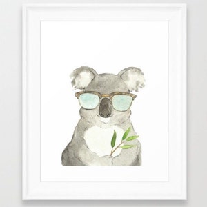 May include: Watercolor painting of a koala wearing sunglasses and holding a sprig of leaves. The koala is gray with a white chest and has brown-framed glasses with blue lenses. The leaves are green, and the artwork is framed in white.