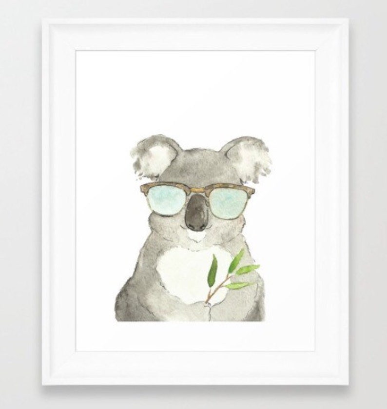 May include: Watercolor painting of a koala wearing sunglasses and holding a sprig of leaves. The koala is gray with a white chest and has brown-framed glasses with blue lenses. The leaves are green, and the artwork is framed in white.