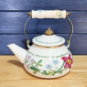May include: White enamel teapot with a floral design featuring pink, purple, and blue flowers. The teapot has a gold trim and a white porcelain handle.