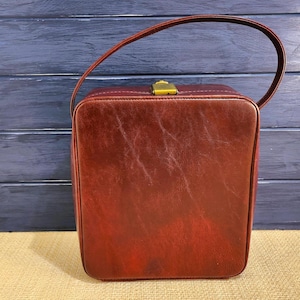 May include: A burgundy leather handbag with a top handle and a gold clasp.