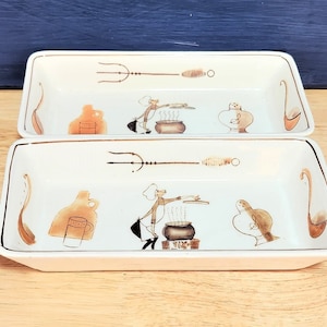 May include: Two white rectangular ceramic serving dishes with brown painted designs. Each dish features a chef figure, a pot, a pitcher, a cup, and a trident. The dishes are ideal for serving appetisers or snacks.