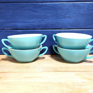 May include: Set of six turquoise ceramic soup bowls with handles. The bowls are stacked in pairs on a wooden surface.