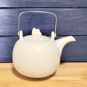 May include: A white ceramic teapot with a silver handle and a small white knob on the lid. The teapot has a textured, rippled surface.
