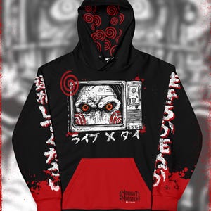 May include: Black hooded sweatshirt with a red and white graphic of a character from the horror movie Saw. The graphic features the character's face in a television screen with the text "Live X Die" and "ライフ X デス" in Japanese. The sleeves have a red and black splatter pattern with the text "Live X Die" and "ライフ X デス" in Japanese. The hoodie has a red pocket and the text "Midnight's Monster" on the pocket.
